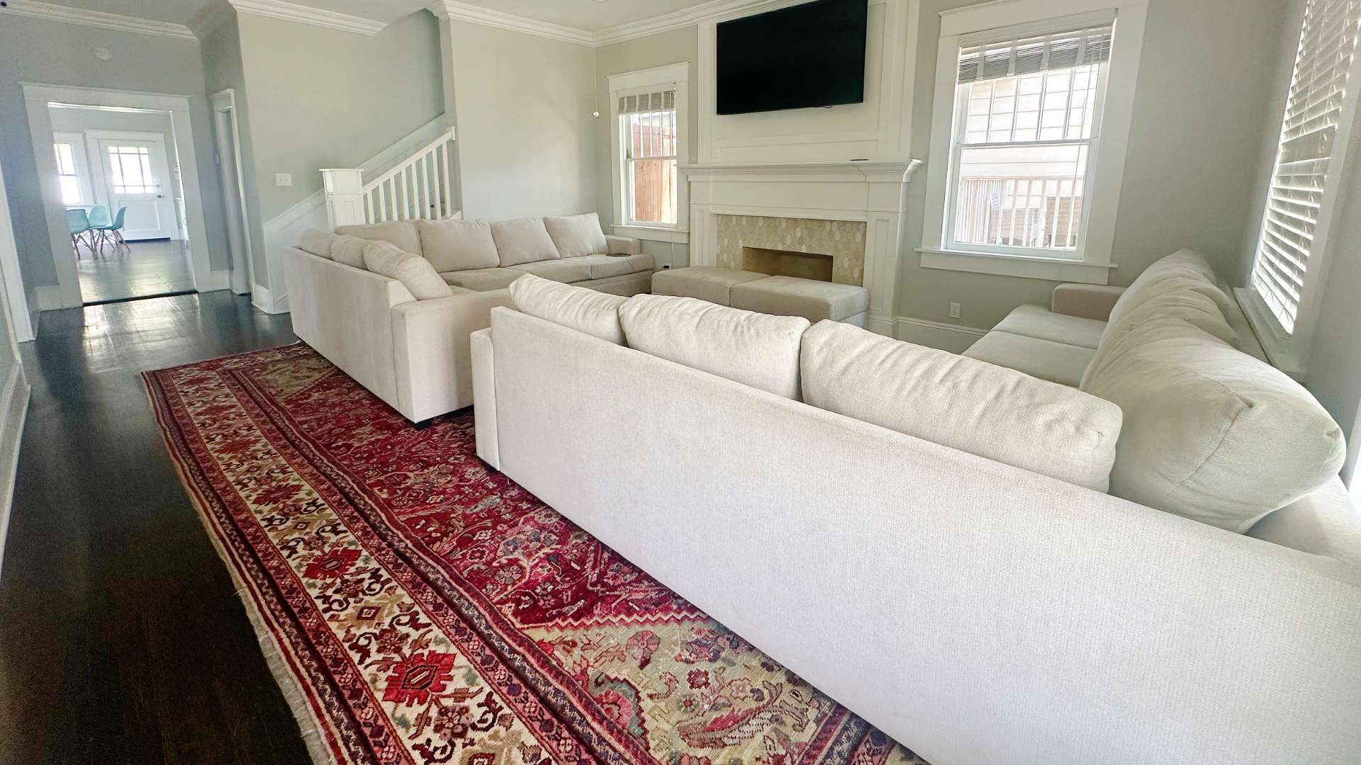 Bright living room with a white sectional sofa, fireplace, and wall-mounted TV; a red oriental rug runs along the dark wood floor.