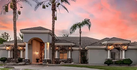 Luxurious single-story house with palm trees, stone accents, and a warm sunset sky above the facade.