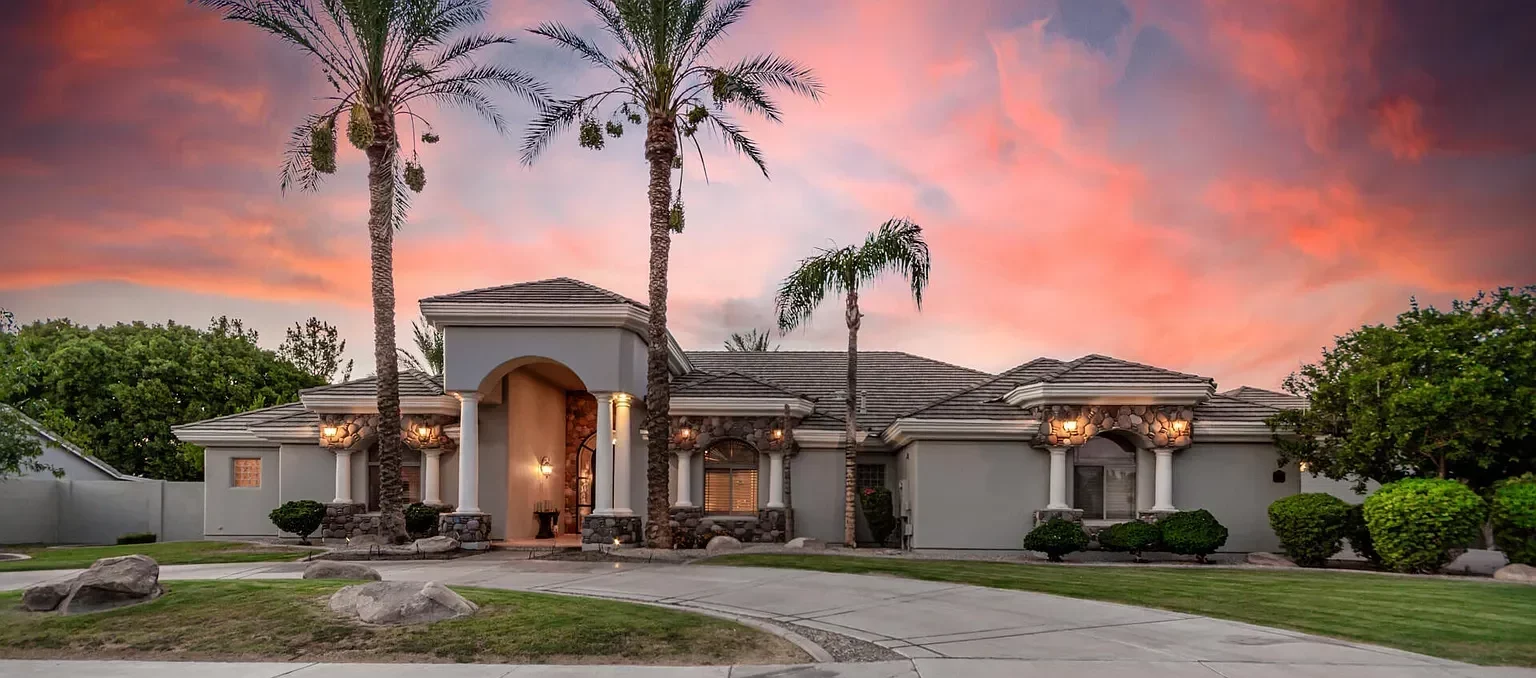 Luxurious single-story home with stone accents, columns, and a curved entry under a pink sunset calm sky.