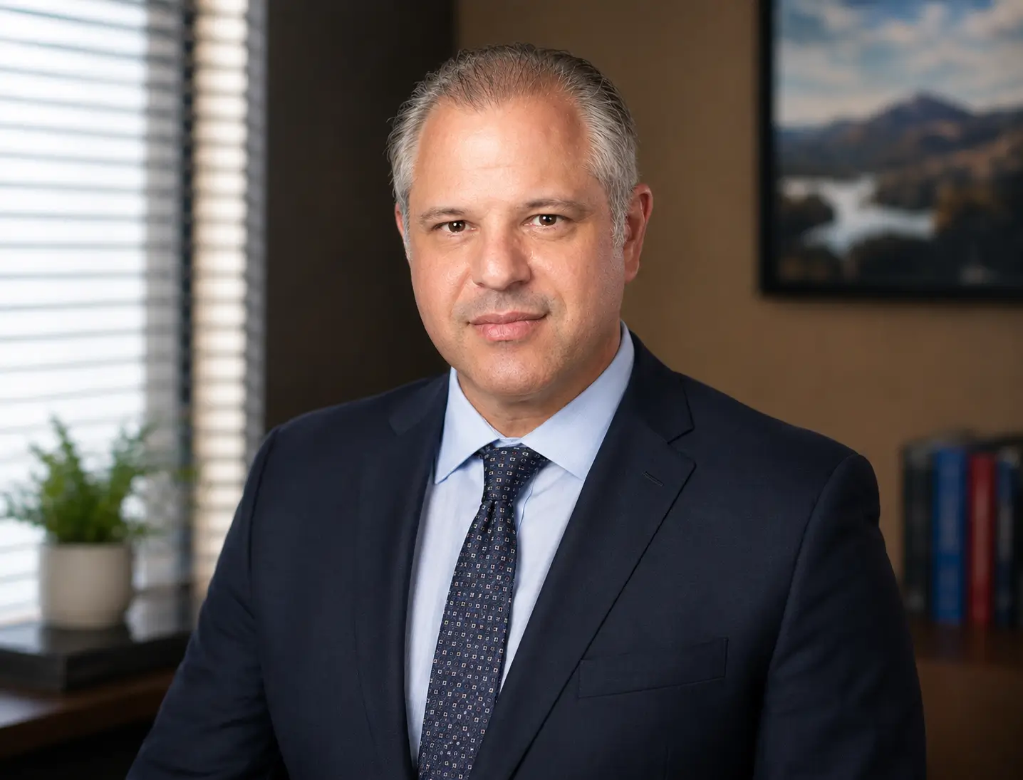 Professional portrait of a middle-aged man in a navy suit and blue tie in an office setting.