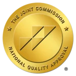 Gold medal badge with diagonal ribbon and the text The Joint Commission National Quality Approval on the rim.